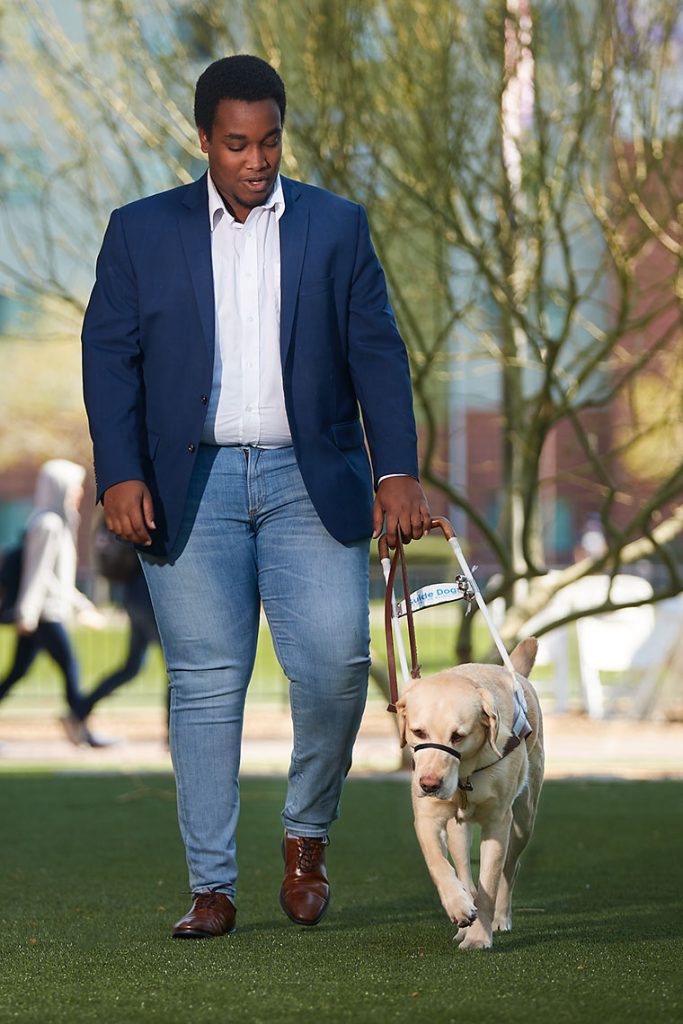 A person with their service animal on a lawn at GCU.