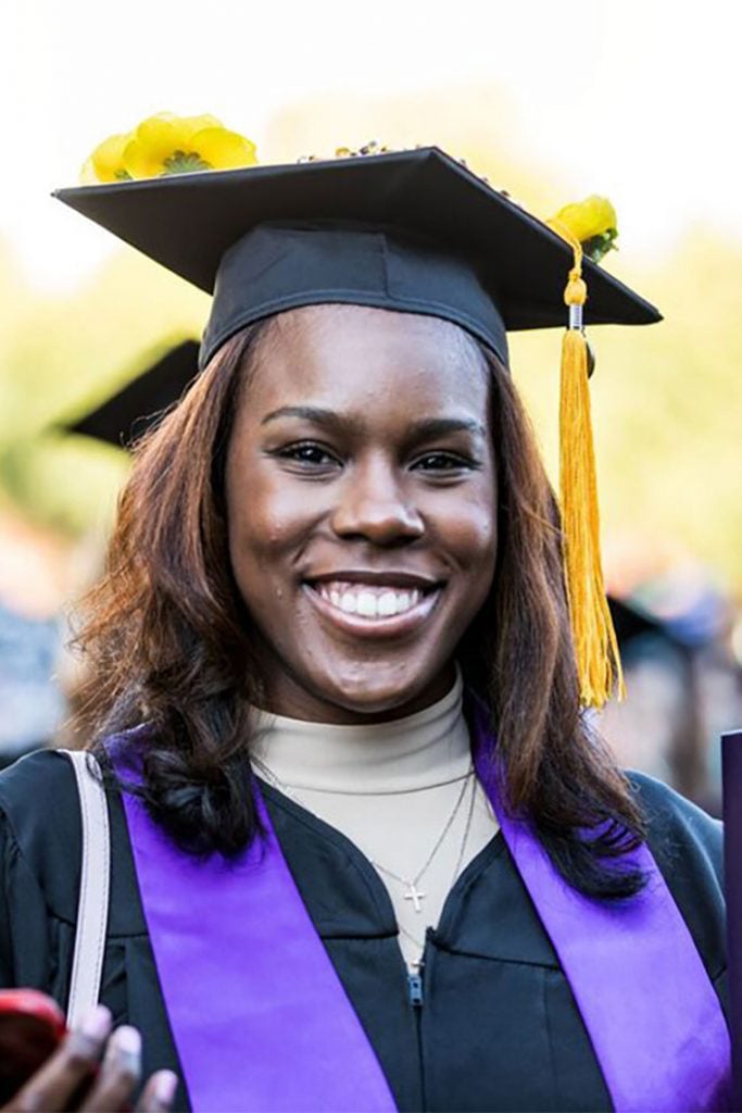 GCU Graduate smiling and wearing GCU cap and gown