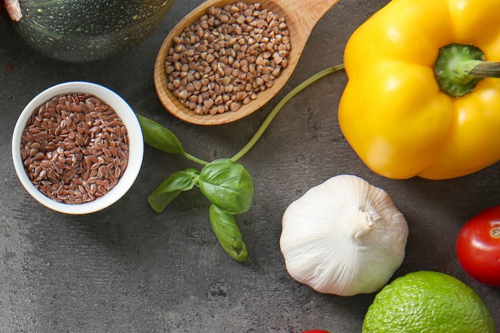 Above view of two bowls of grain, yellow pepper, basil and garlic on a gray table. 