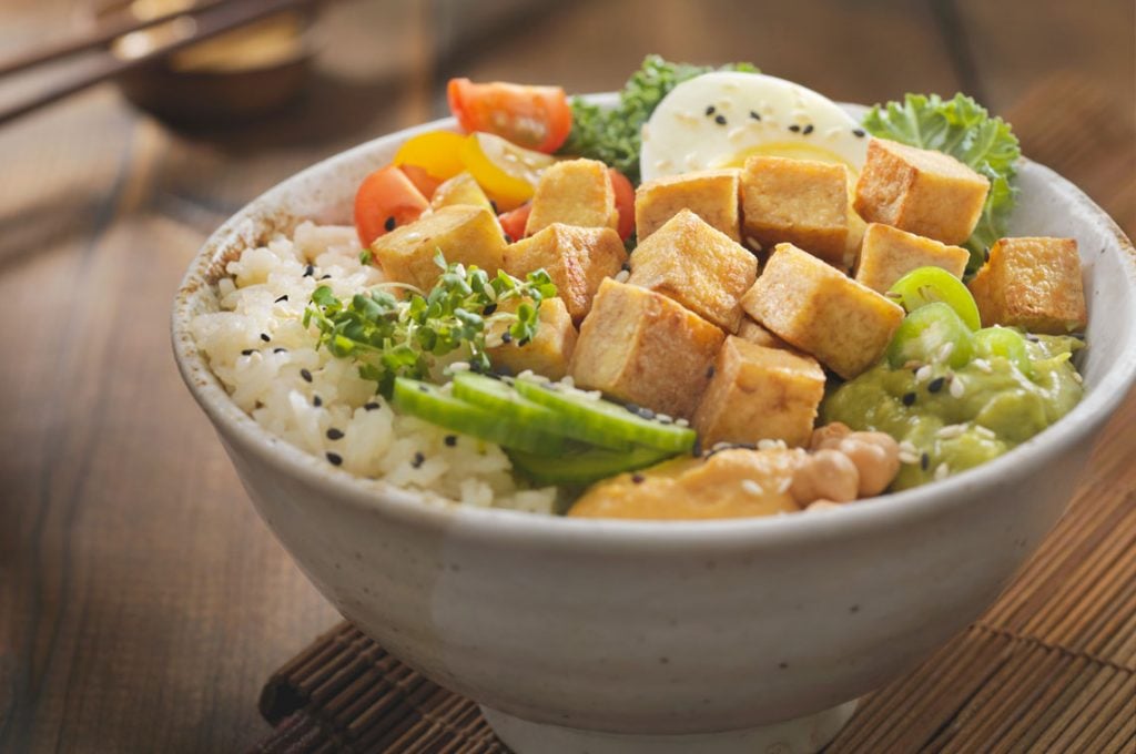 Picture of a bowl of chicken, mixed vegetables and rice on a table.